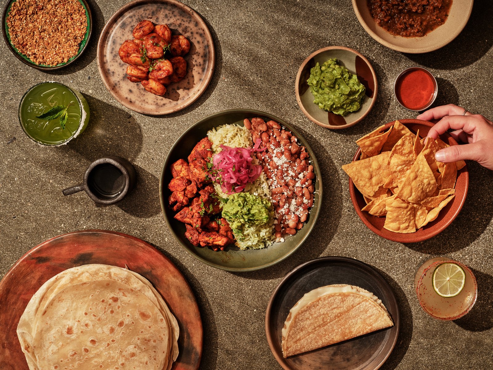 LOQUI chicken bowl surrounded by shrimp, guacamole, tortilla chips, tortillas, and drinks