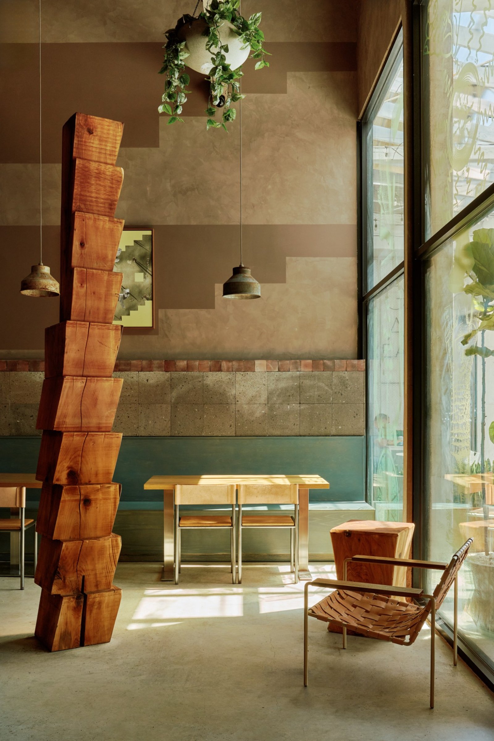 Sunlit LOQUI dining room with a wooden sculpture, hanging plants, and green seating