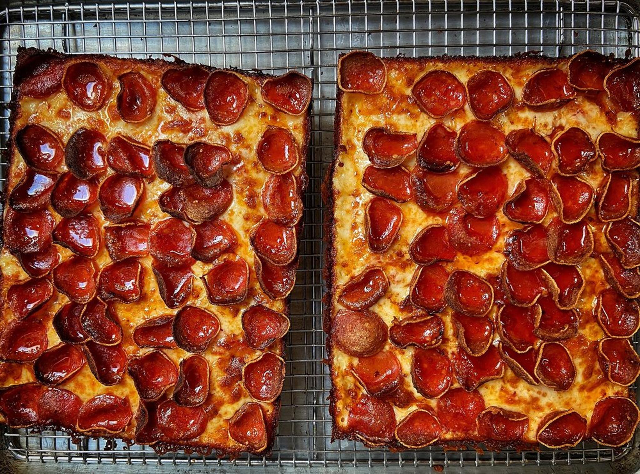 Two rectangular pepperoni pizzas on a wire cooling rack.