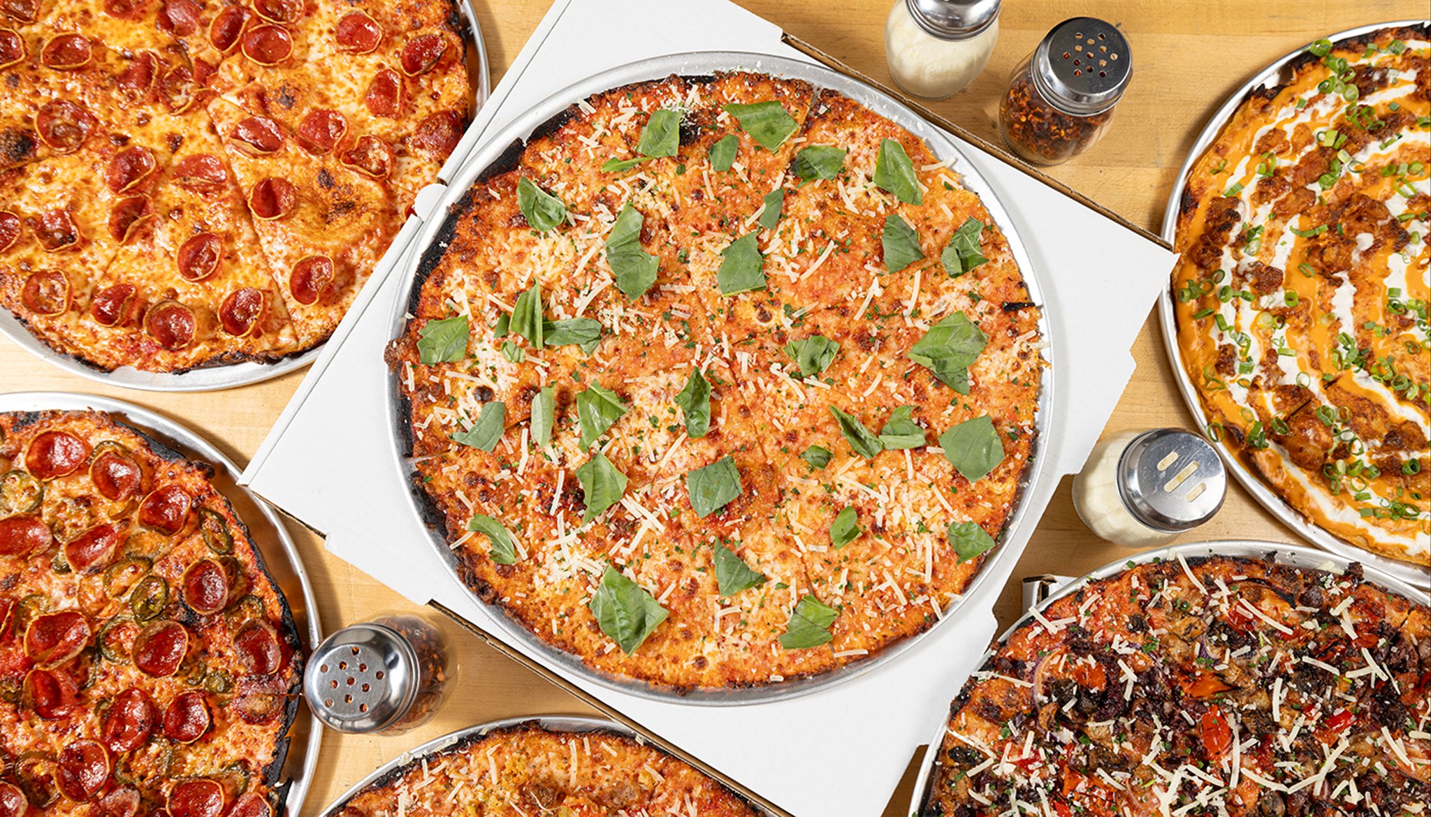 A spread of thin, crispy bar-style pizzas from Bar Pie Guys on metal trays