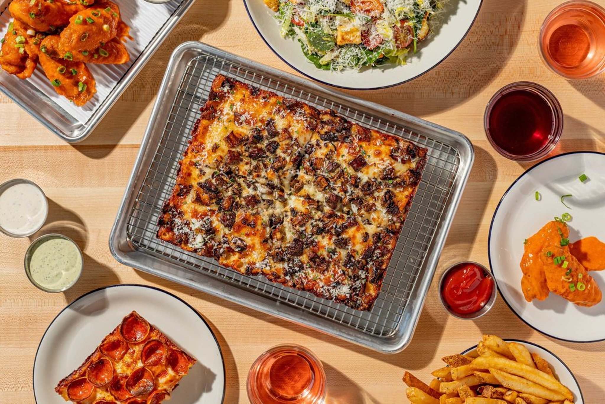 Overhead view of a pizza with chopped bacon on top, surrounded by various side dishes including fried chicken, pizza slices, French fries, salad, and drinks.
