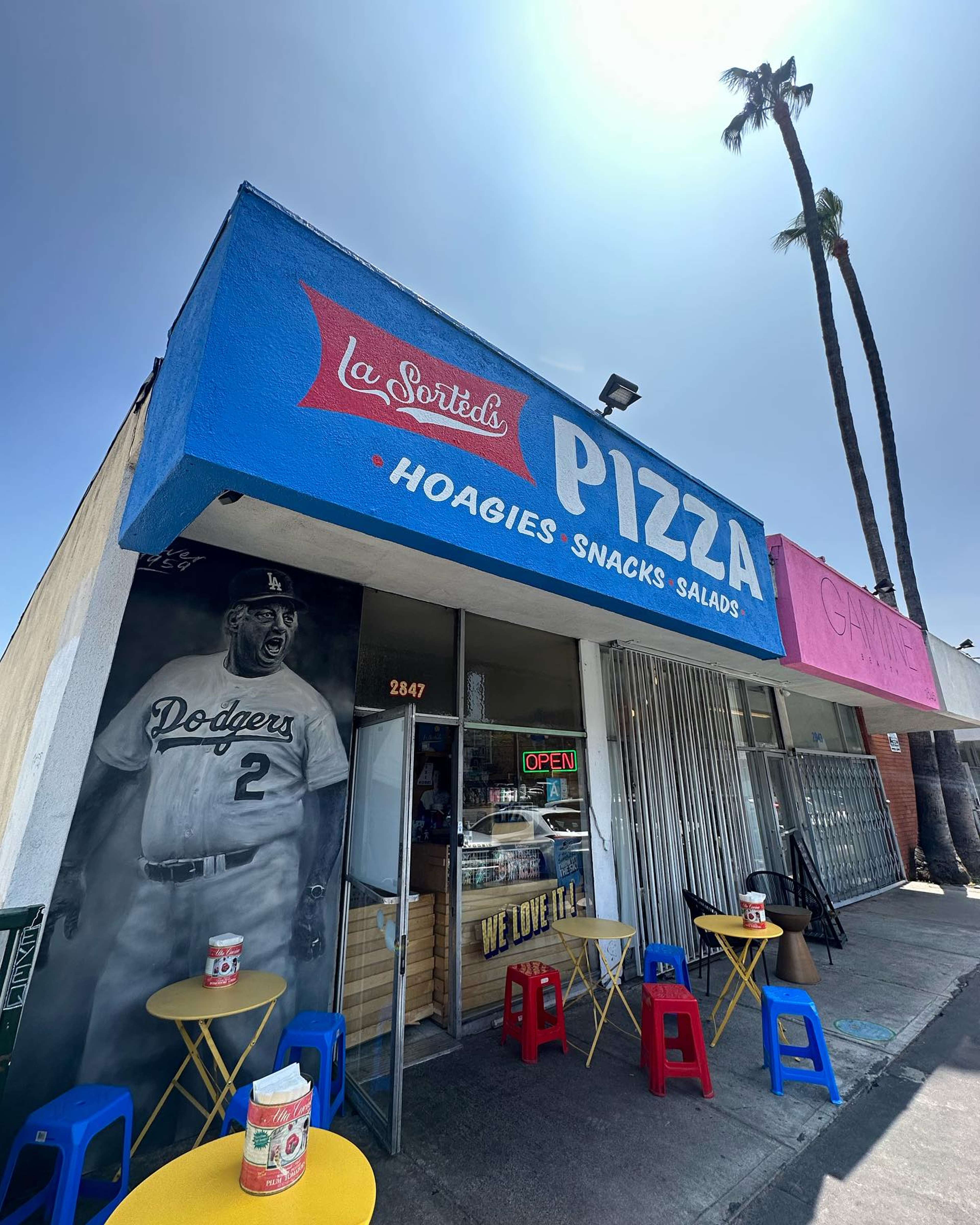 La Sorted's Pizza storefront with outdoor yellow tables, red and blue stools, and a mural of a Dodgers player wearing jersey number 2.