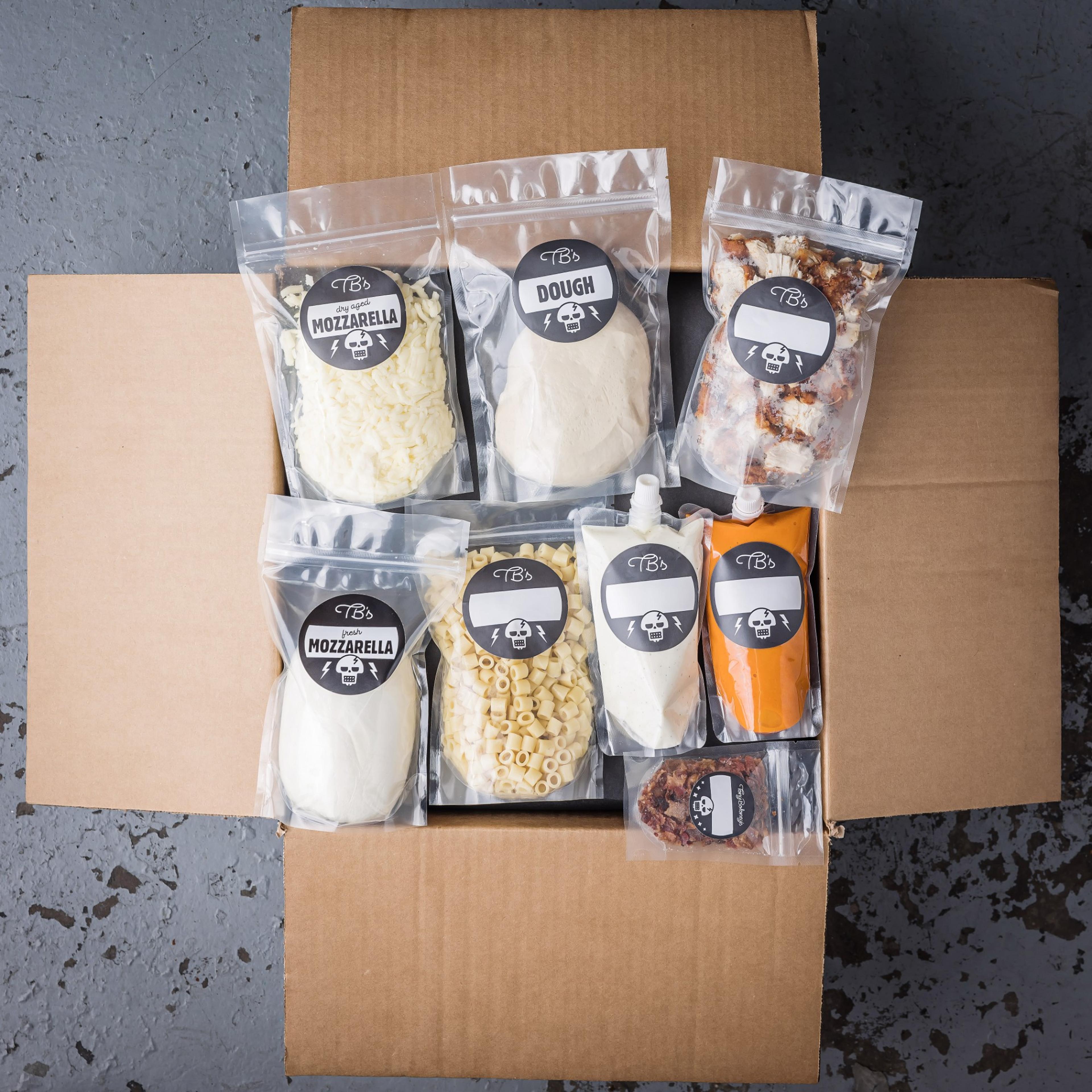 An open Tony Boloney's kit box with labeled bags of dough, mozzarella, sauces, and toppings