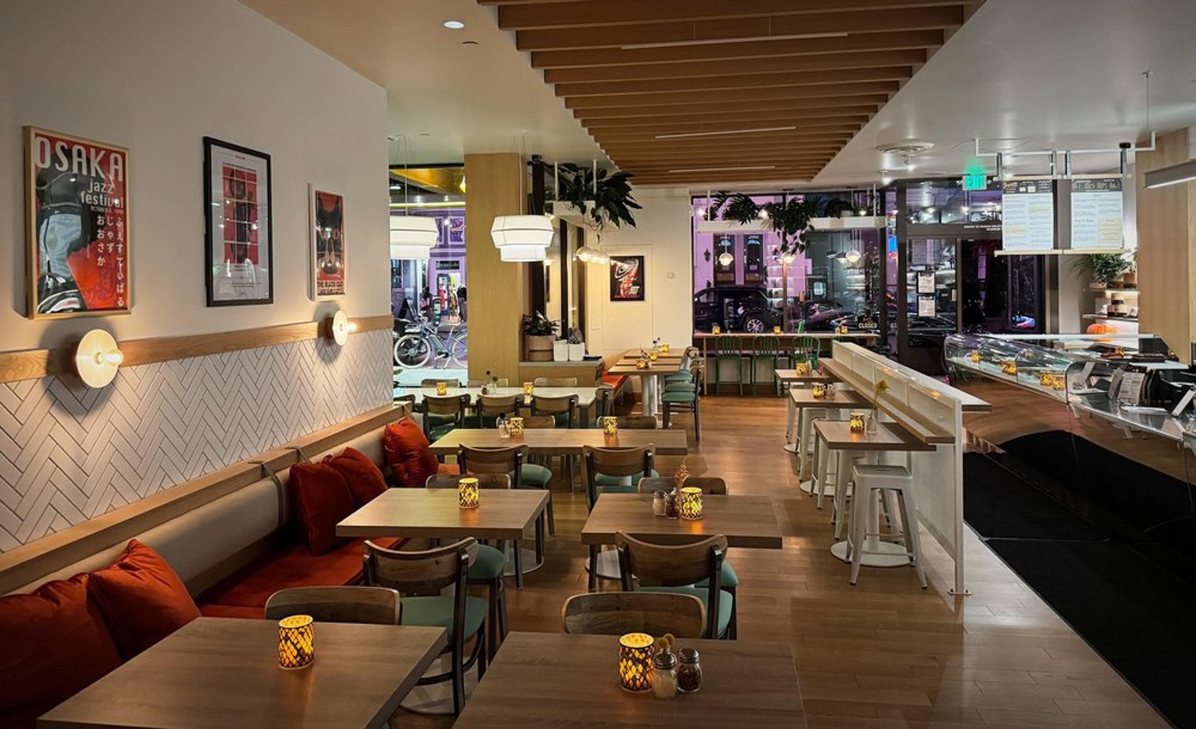 Interior of a Joyride Pizza in the Marina with a cozy interior with wooden tables and chairs, lit candles on tables, a bar counter on the right, artwork on the walls, and large windows showing a street scene outside.
