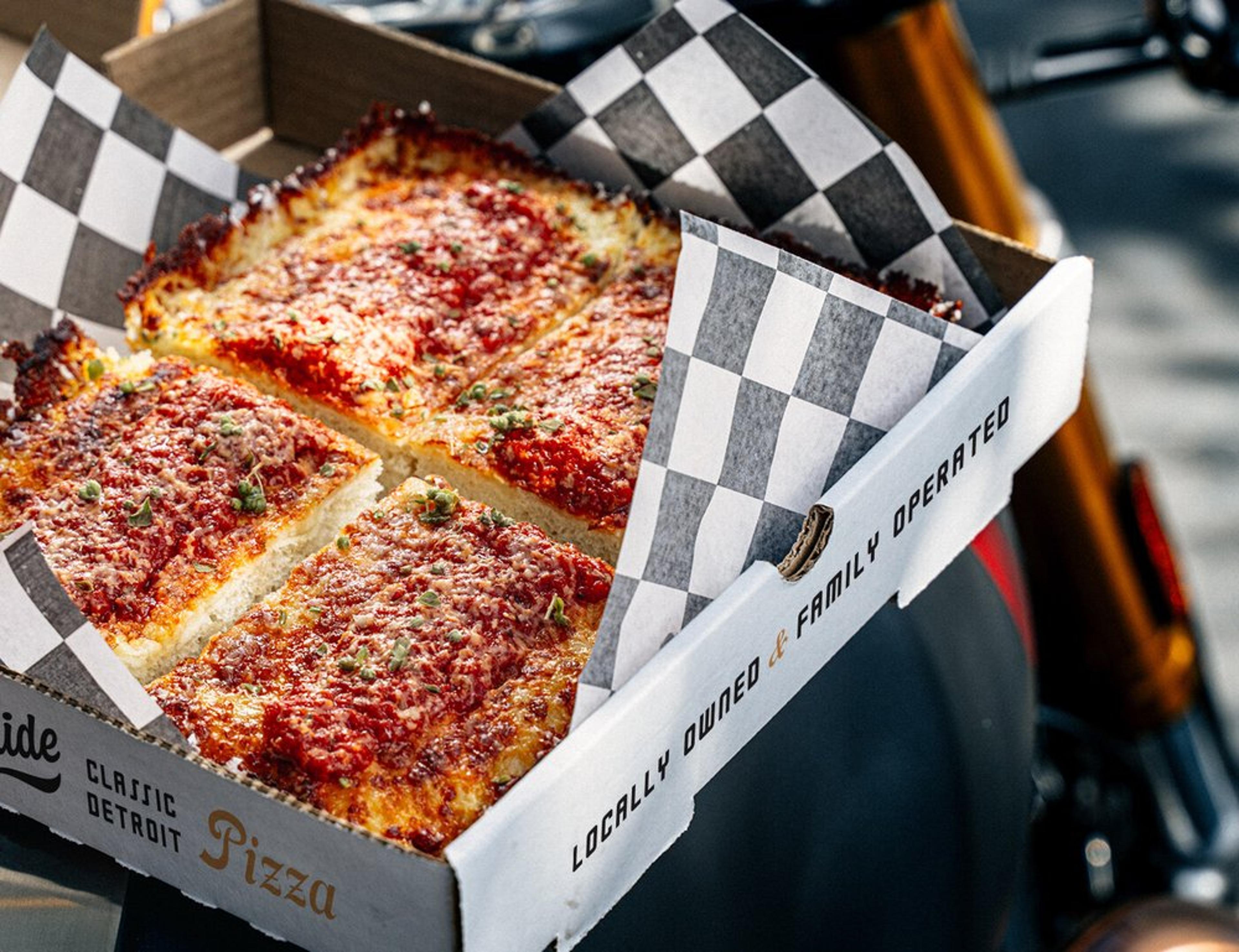 A box of Detroit-style pizza with a thick, cheesy crust and tomato sauce.