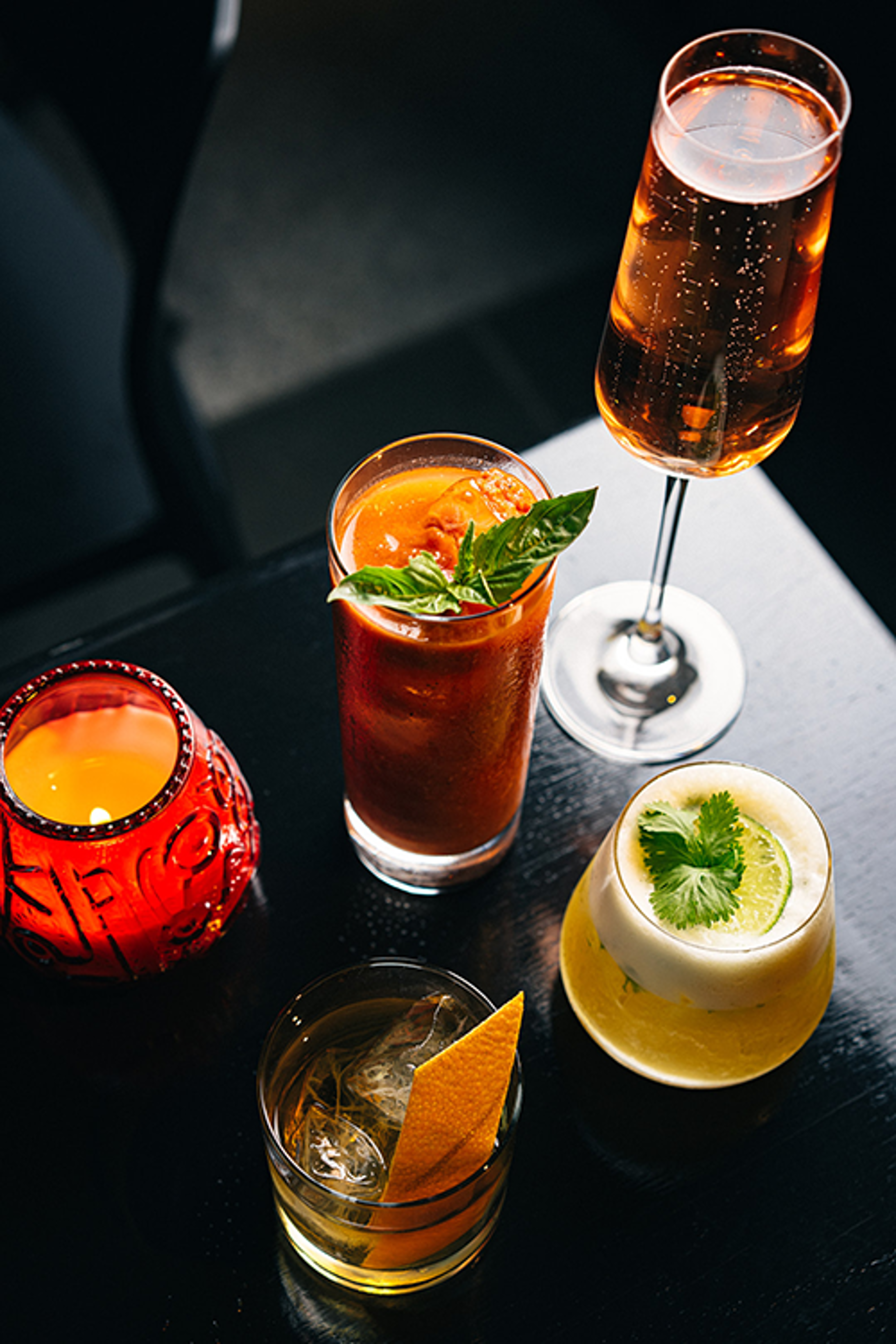 Colorful cocktails, a glass of sparkling wine, and a whiskey drink on a dark table.