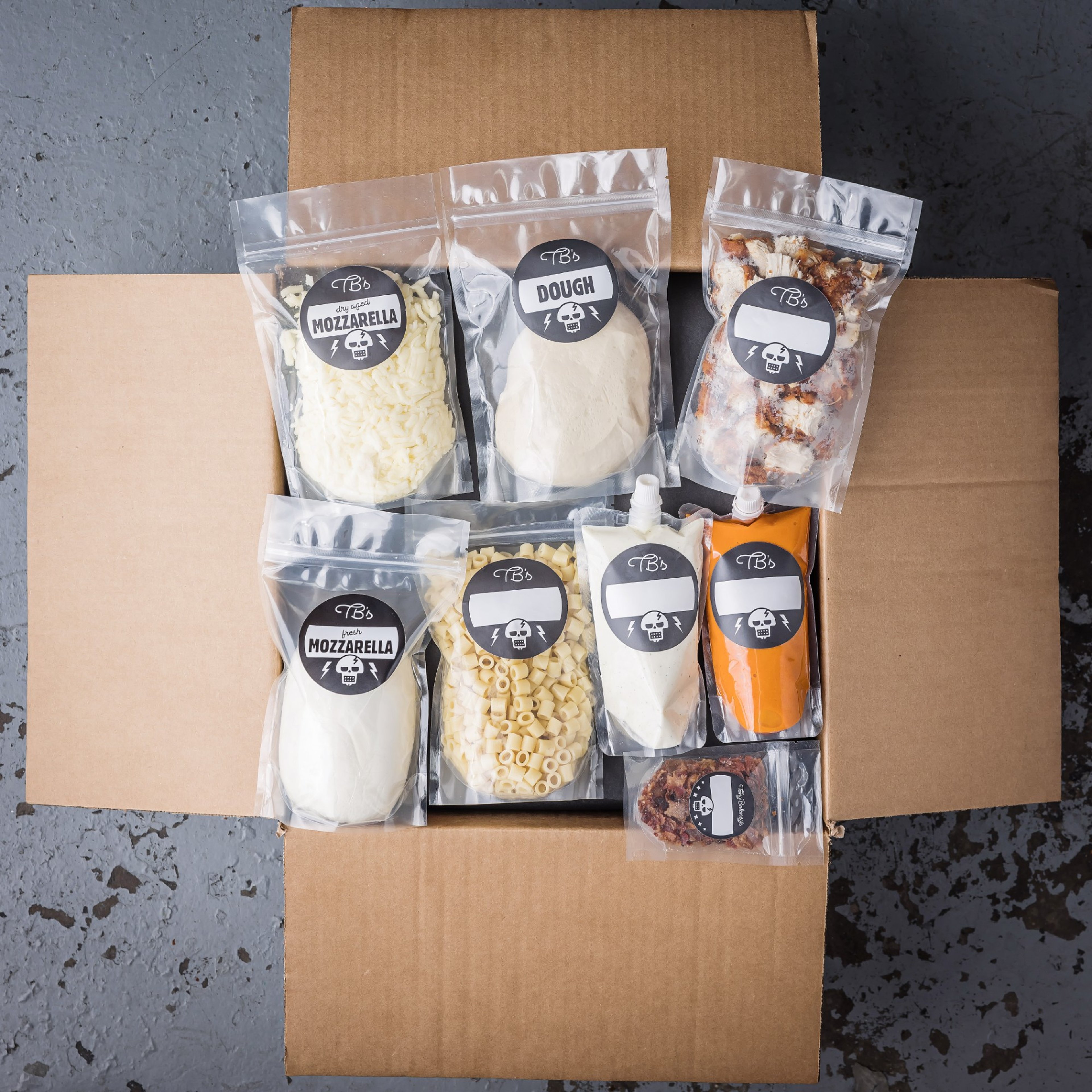 An open Tony Boloney's kit box with labeled bags of dough, mozzarella, sauces, and toppings