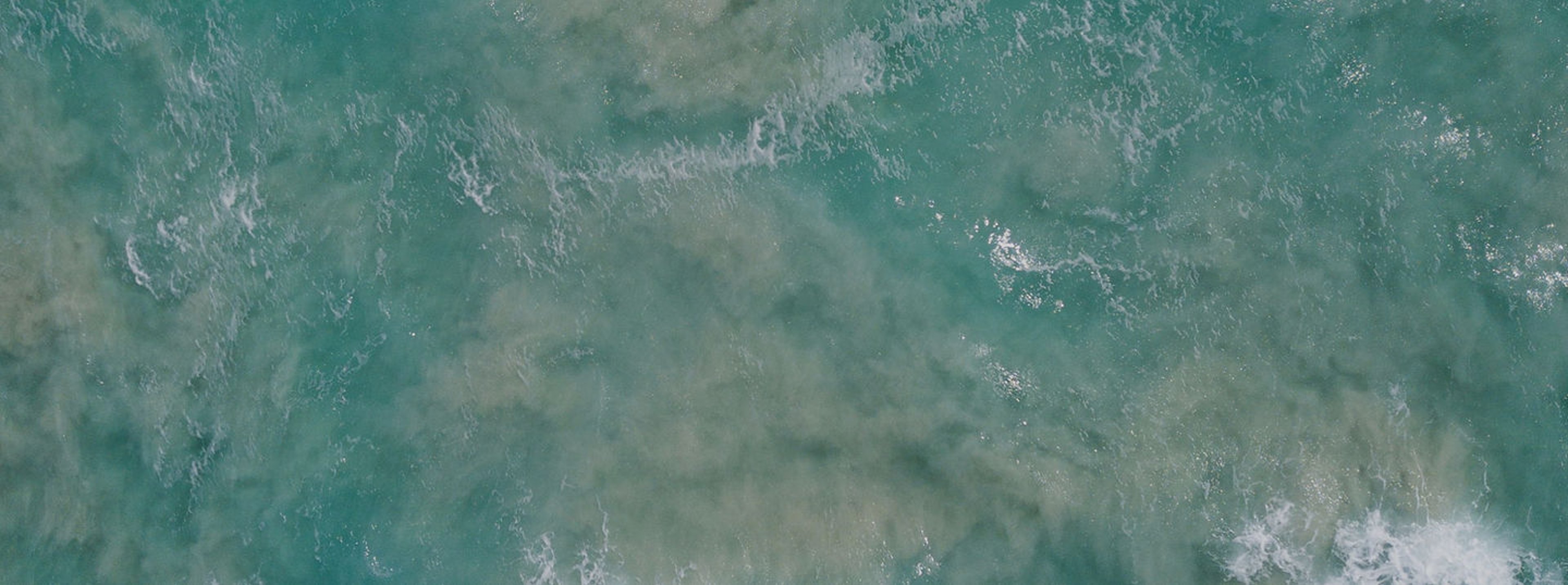 Aerial view of a turquoise ocean wave breaking near the shore