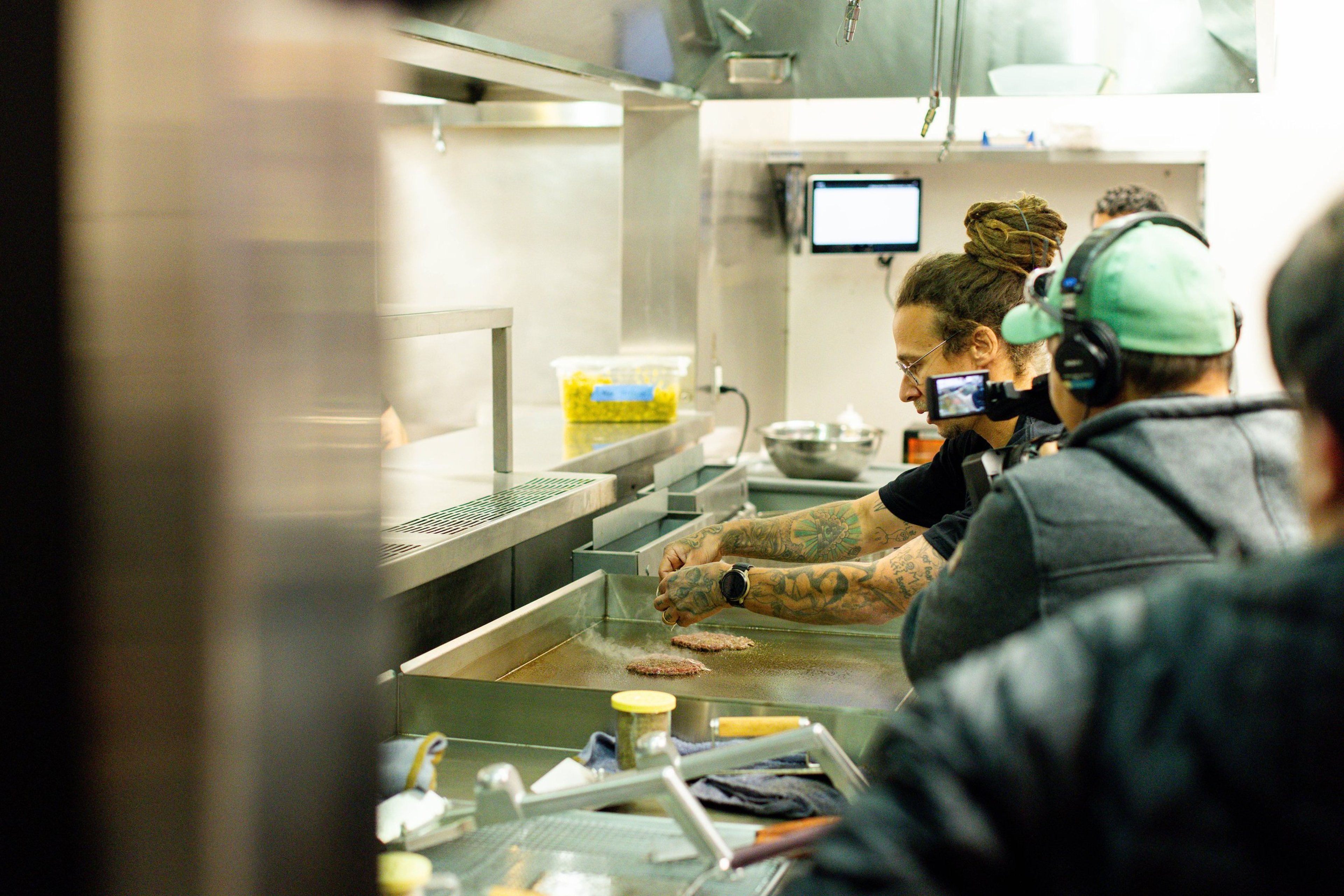Chef with tattoos cooking burger patties on a flat-top grill at the NADC Burger Denver grand opening.
