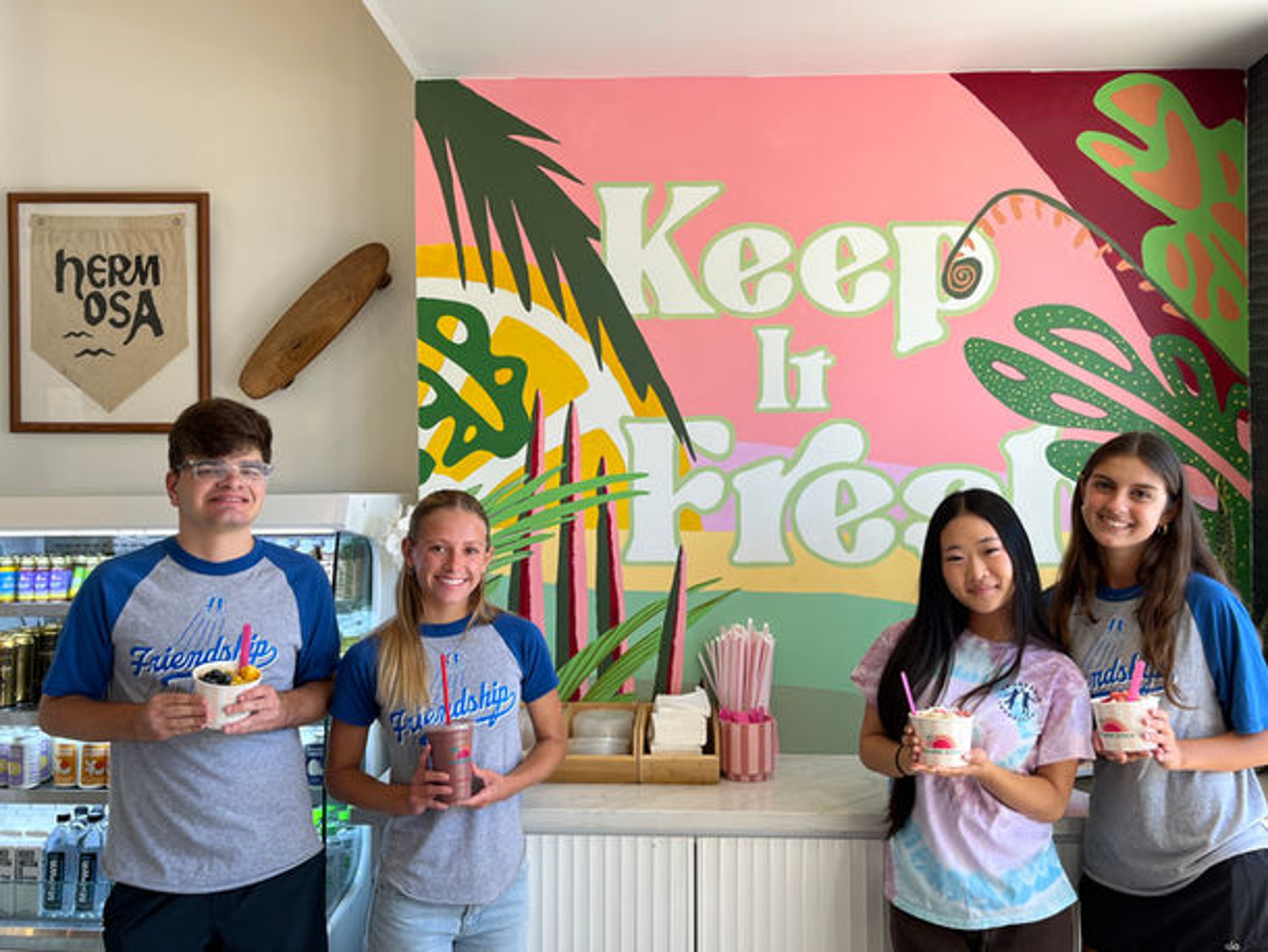 Fundraiser group holding bowls in front of the Keep It Fresh mural inside Paradise Bowls