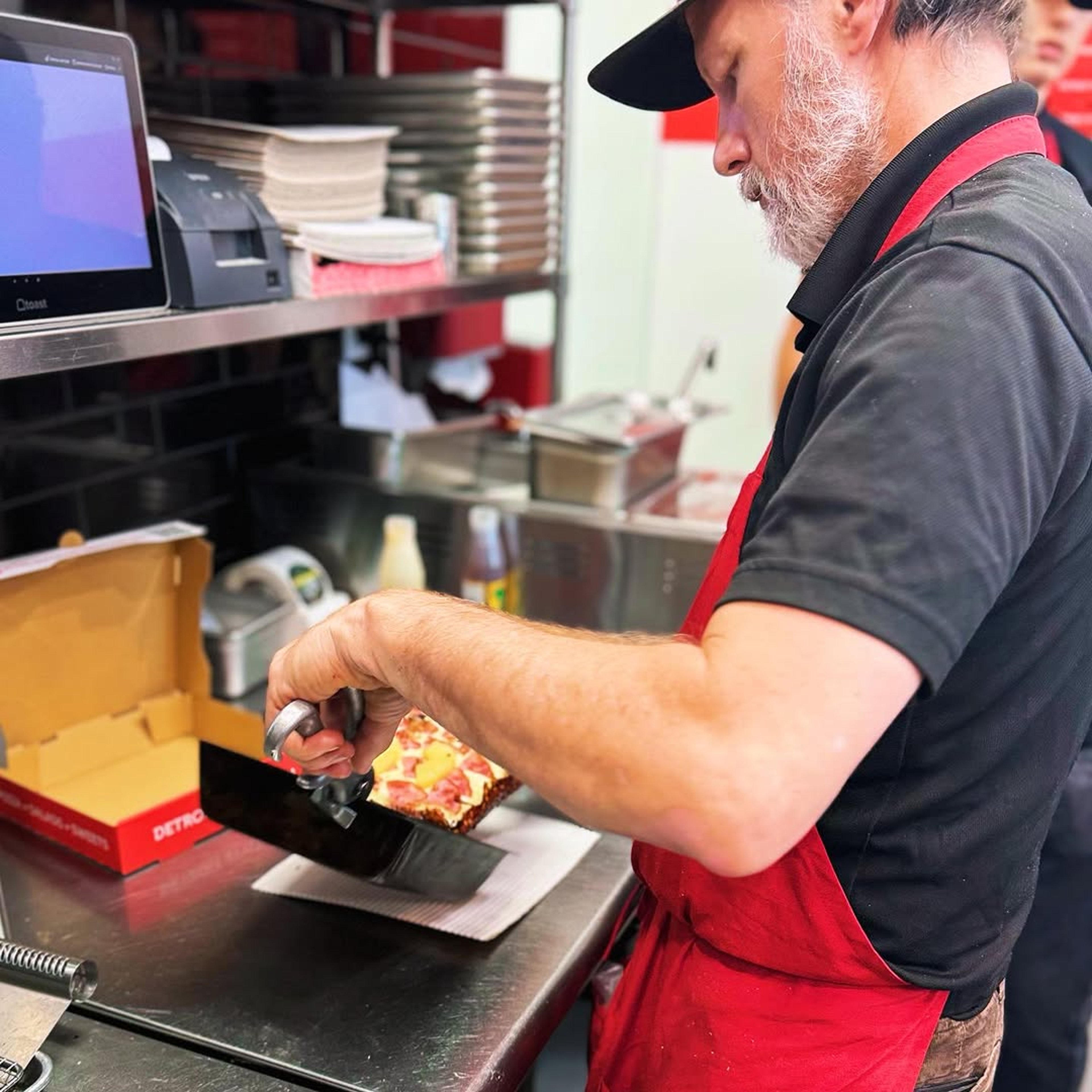 A chef at The Ria Pizzeria preparing a Detroit-style pizza