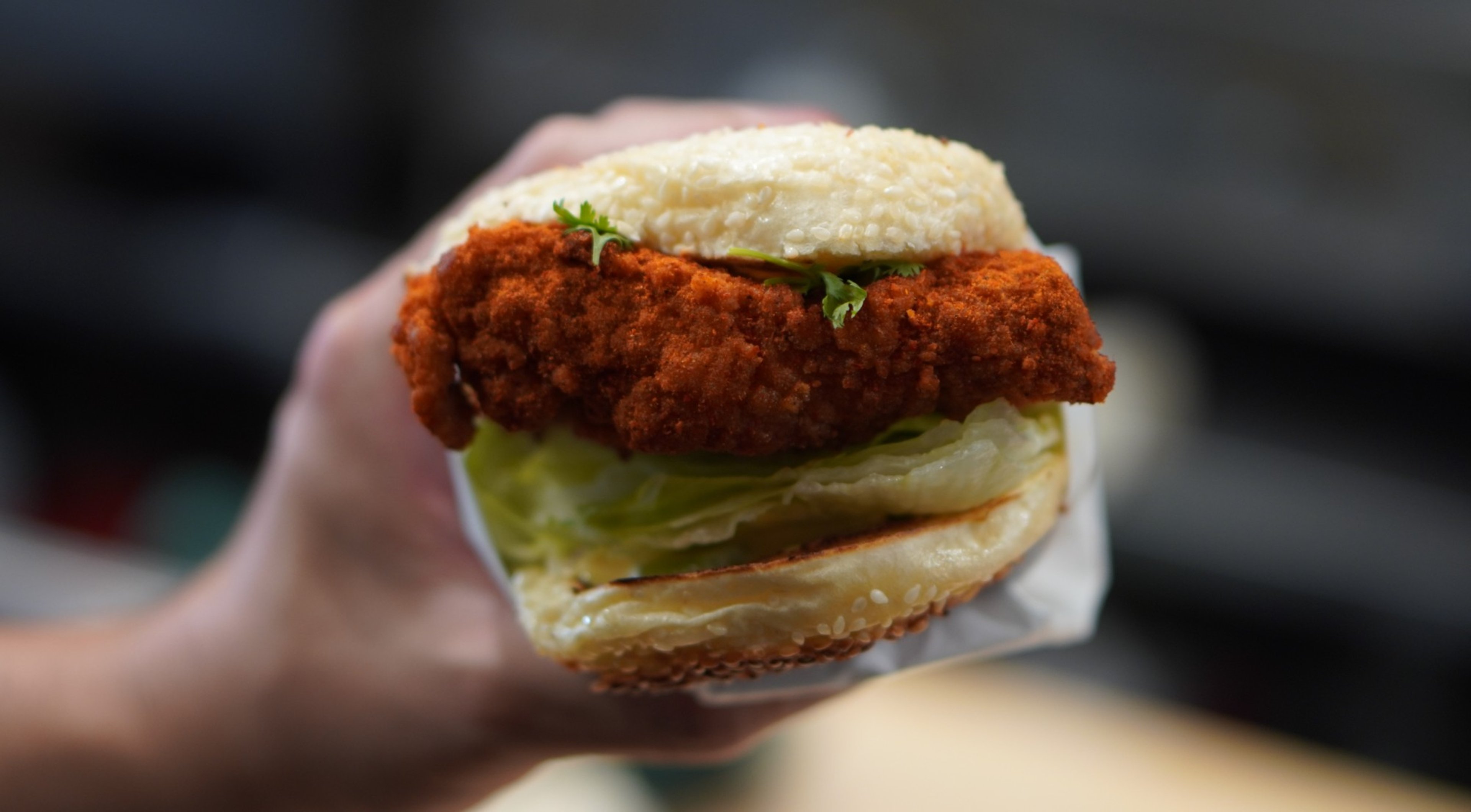 Ok's Deli Sichuan hot chicken sandwich on a sesame bun, held in a hand