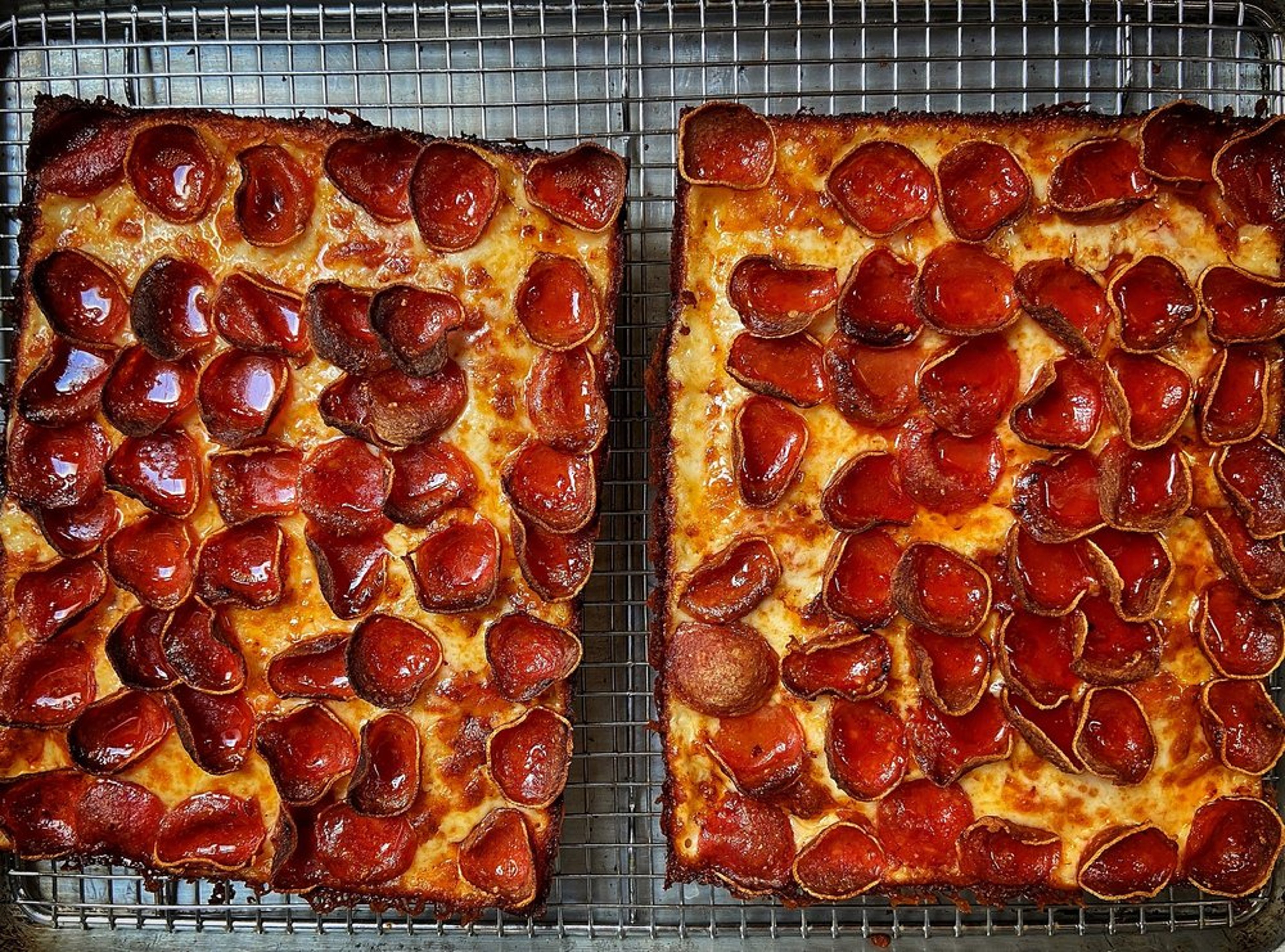 Two rectangular pepperoni pizzas on a wire cooling rack.