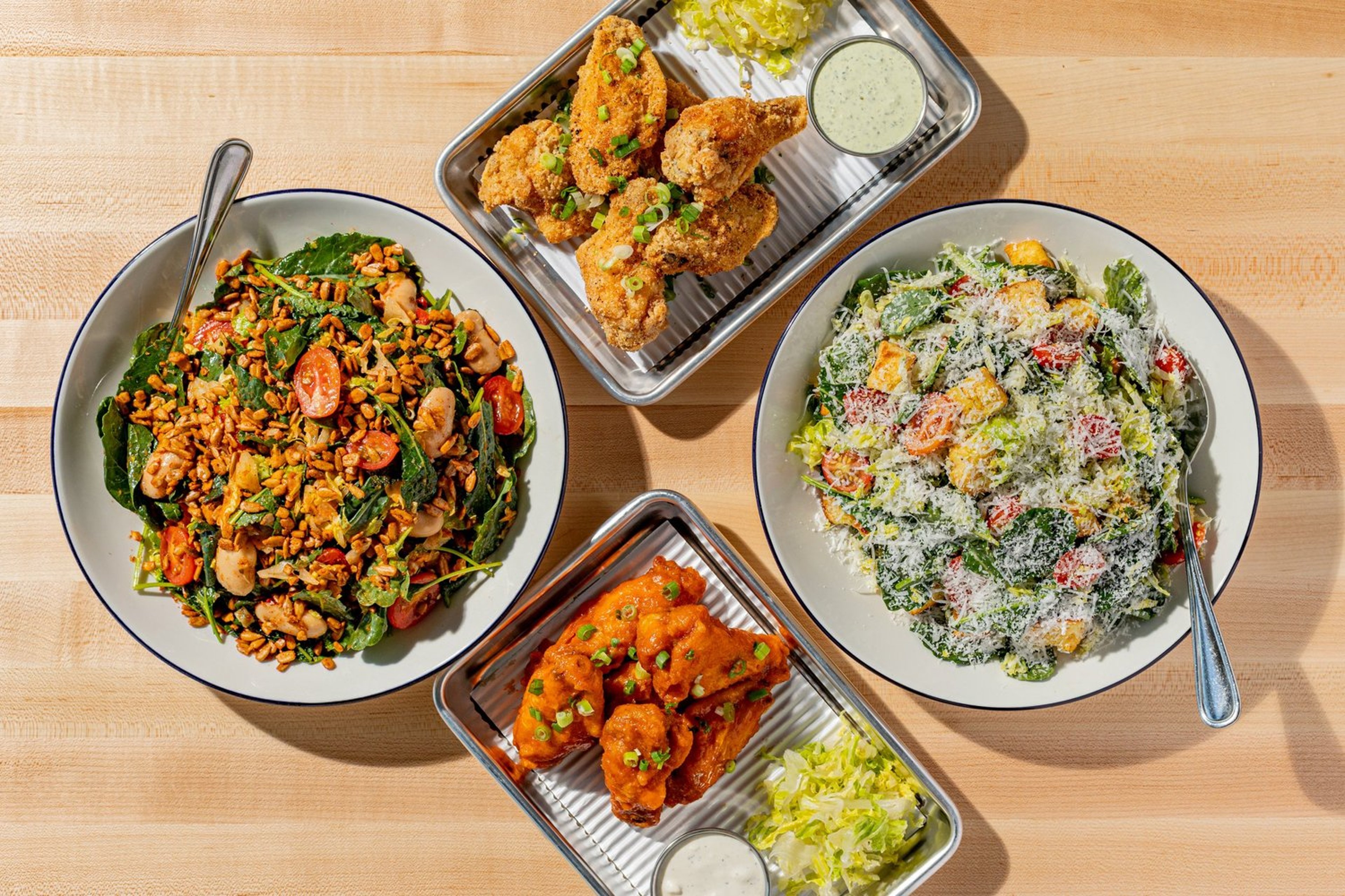 Top-down view of various bowls and plates with salad, fried chicken, pasta salad, and chicken wings