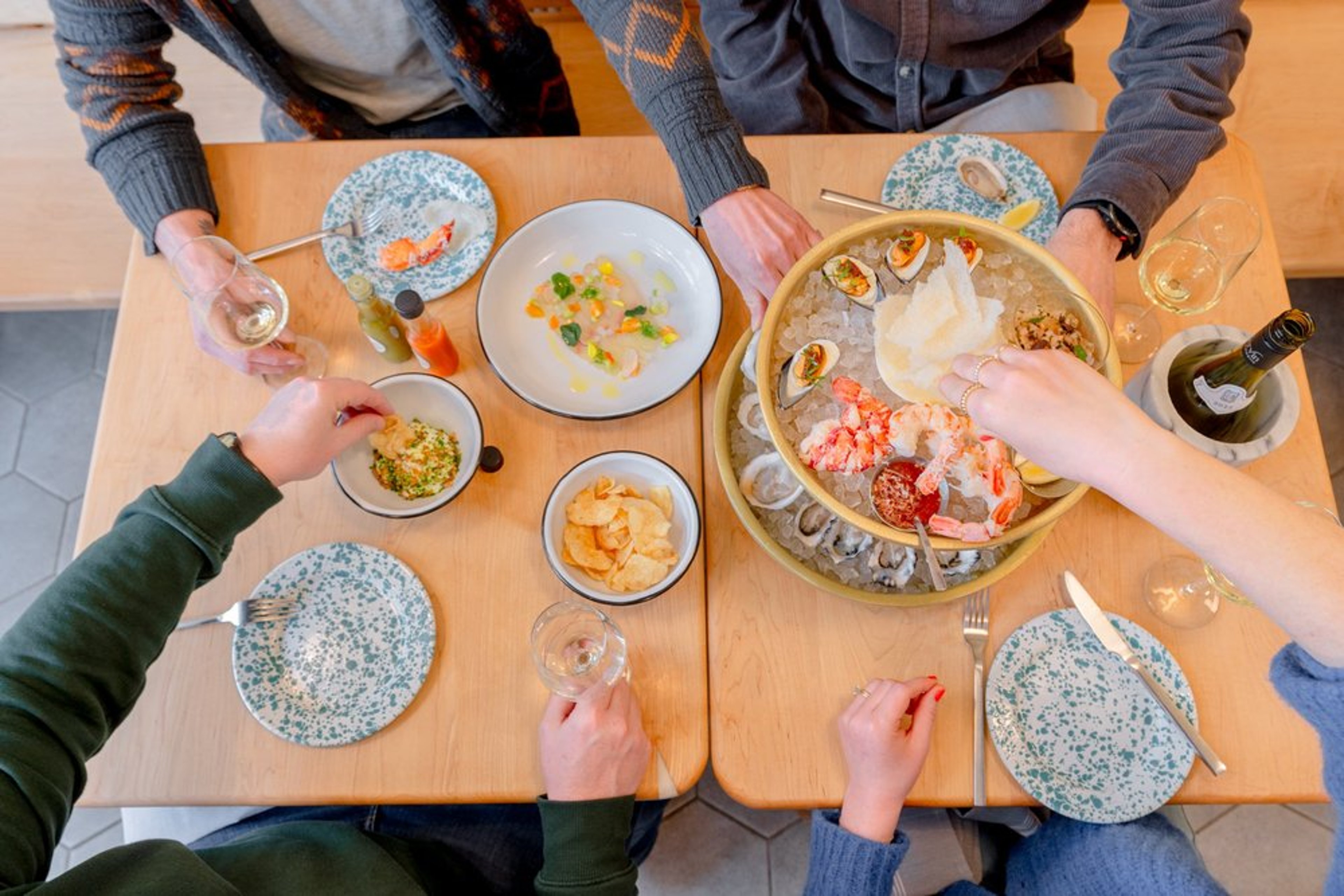 Overhead view of guests sharing a seafood platter with oysters, shrimp, and wine at Little Shucker.