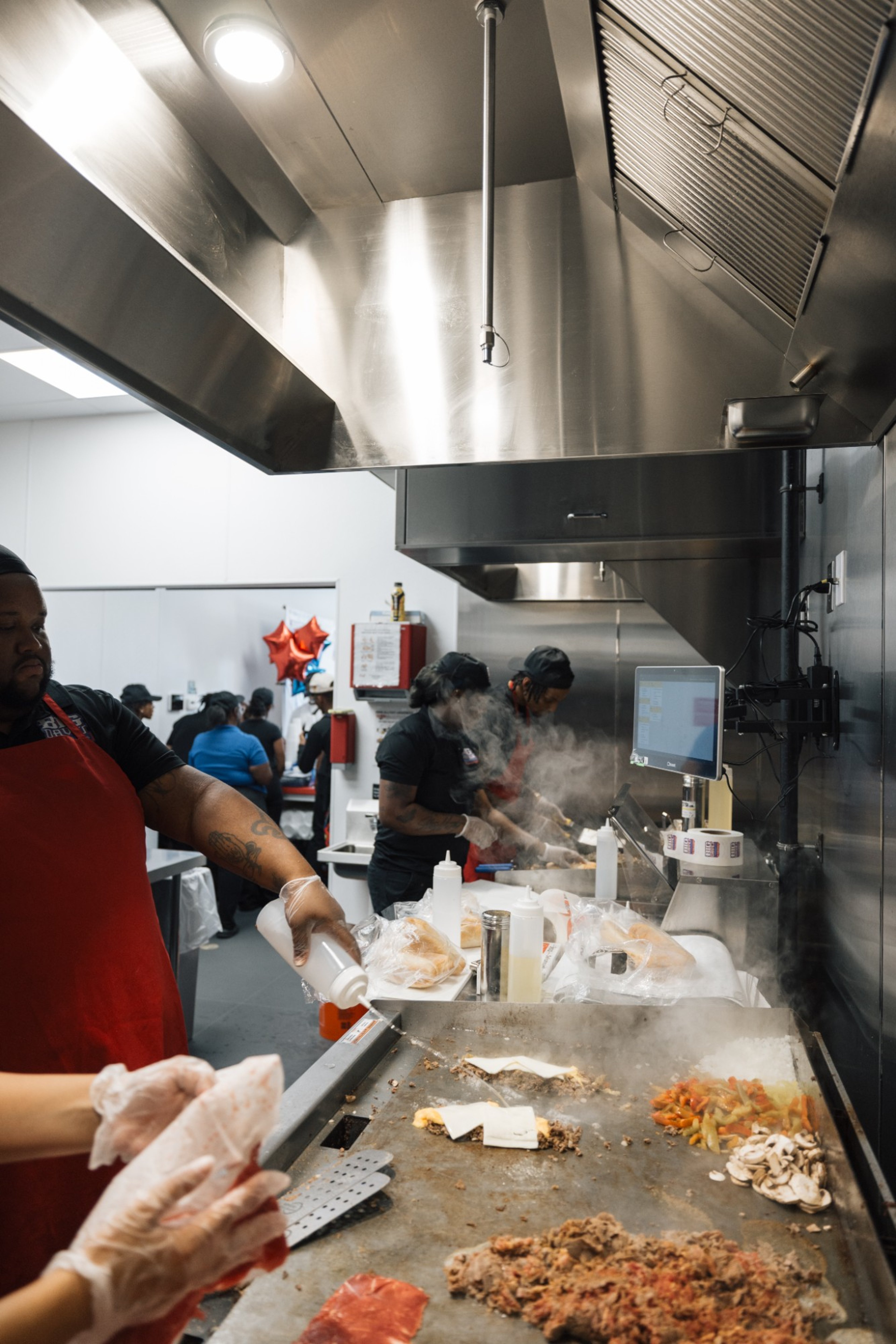 Big Dave's Cheesesteaks team cooking cheesesteaks on the grill in a busy kitchen